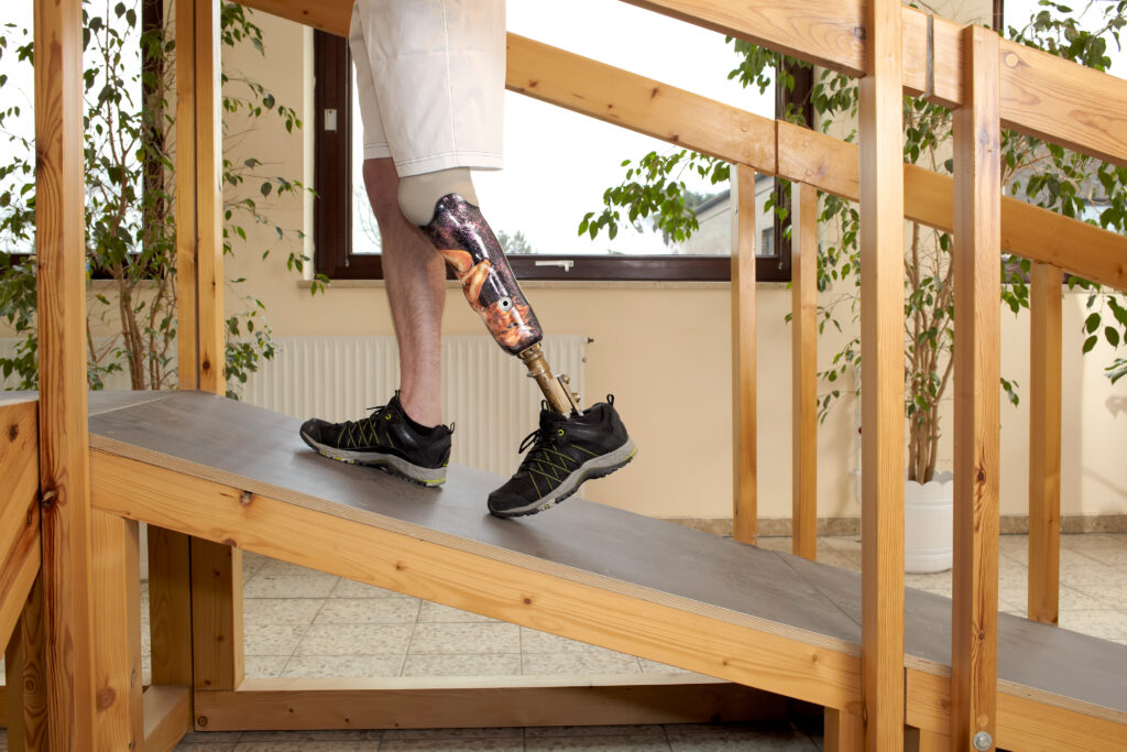 A person with a prosthetic leg walking up a wooden ramp indoors.